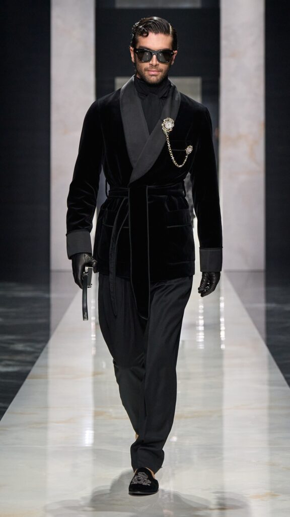 On pensait que la broche resterait au fond des tiroirs de nos grands-mères : en 2026, c'est sur les vestes et les cardigans des hommes qu'elle s'épingle - - dolce and gabbana men fall winter 26 fashion show look 21